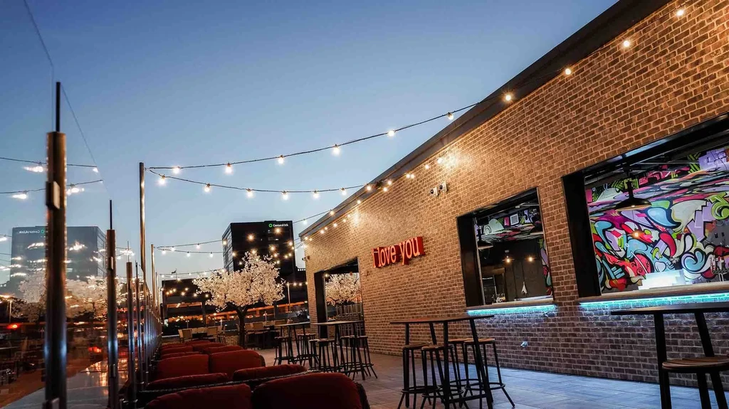 Brick restaurant with "i love you" neon, graffiti, and string-lit evening patio.