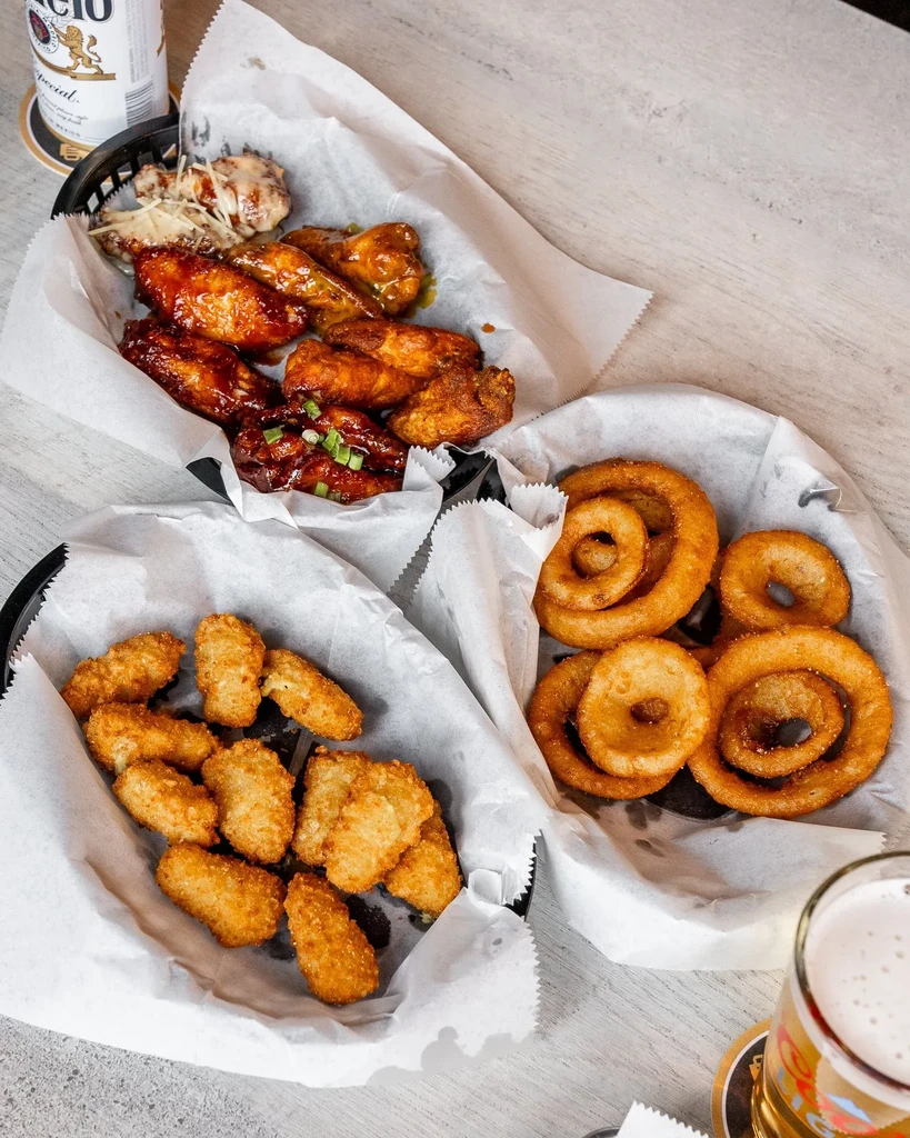 Fried chicken wings, tater tots, onion rings, and beer on a table.