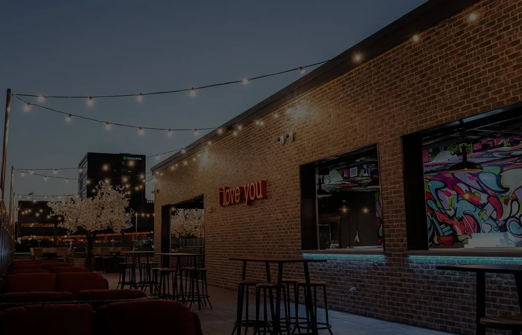 Outdoor patio: brick wall, colorful graffiti, 'love you' neon, string lights.