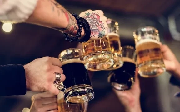 Several hands clinking beer mugs, showing tattoos, in a pub.