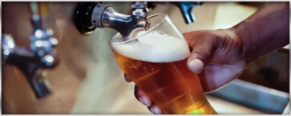 Dark-skinned hand pouring frothy golden beer from a tap.