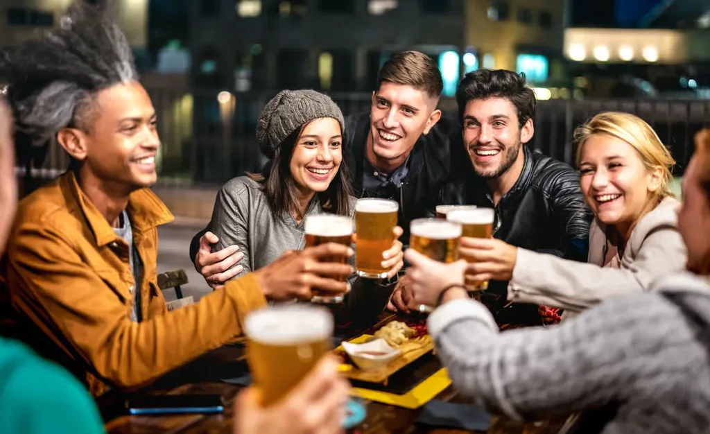 Friends smiling, toasting beer glasses with appetizers at night.