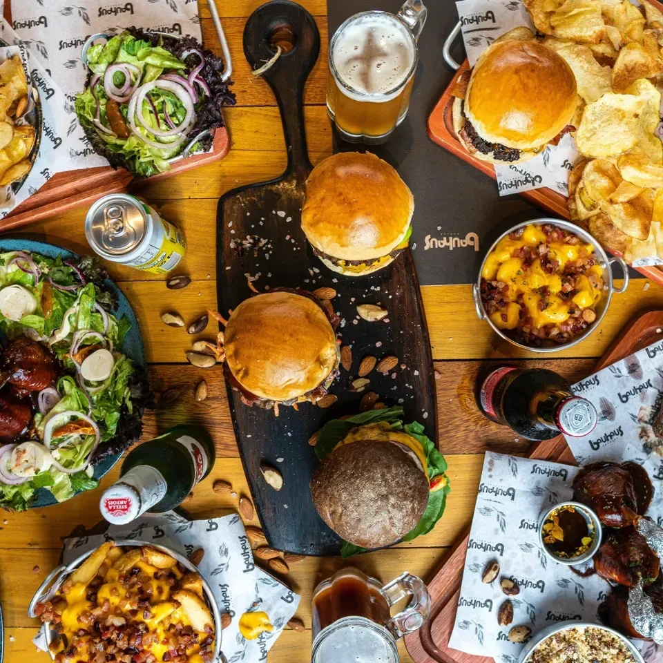 Burgers, loaded fries, salads, and beer spread on a rustic wooden table.