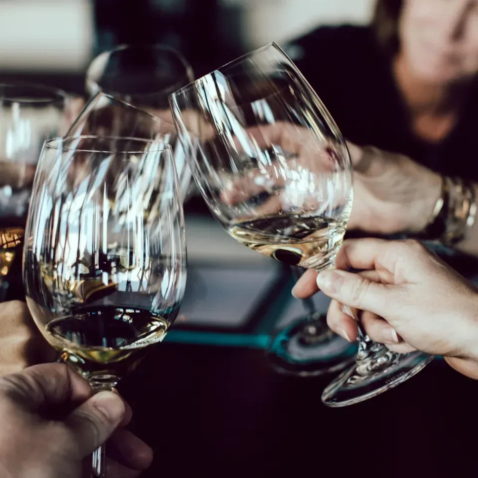 Multiple hands toast with stemmed glasses of white wine.