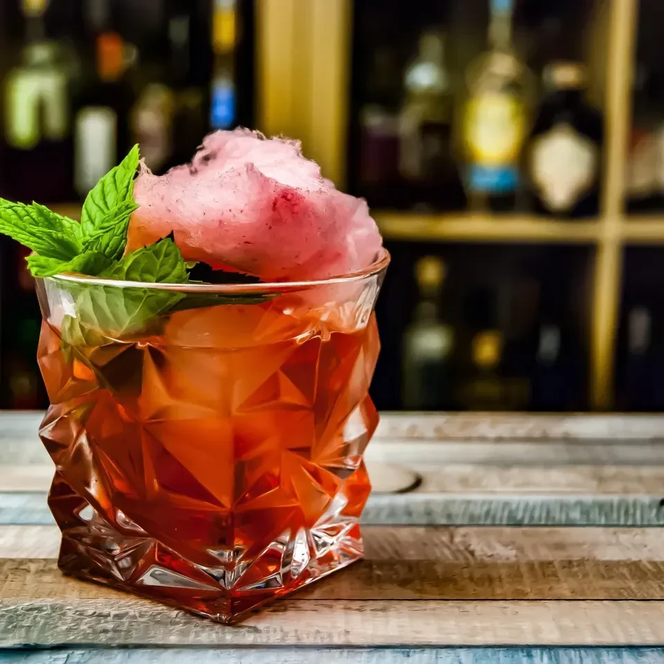 Faceted glass cocktail with cotton candy and mint on a wood bar.