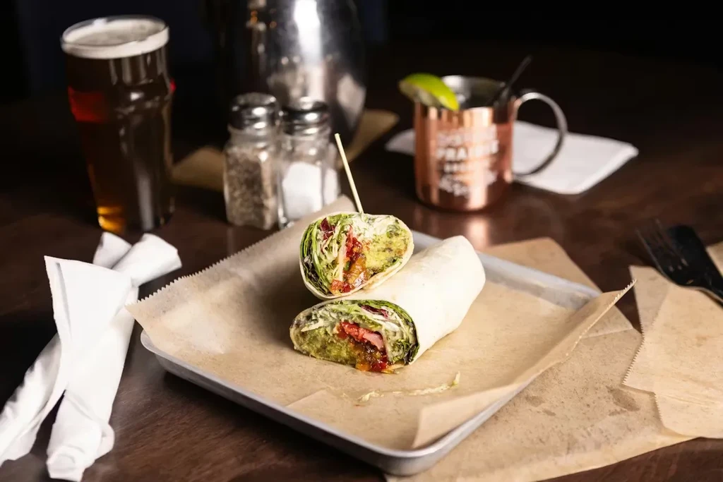 Vibrant wrap, beer, and copper mug on a dark restaurant table.