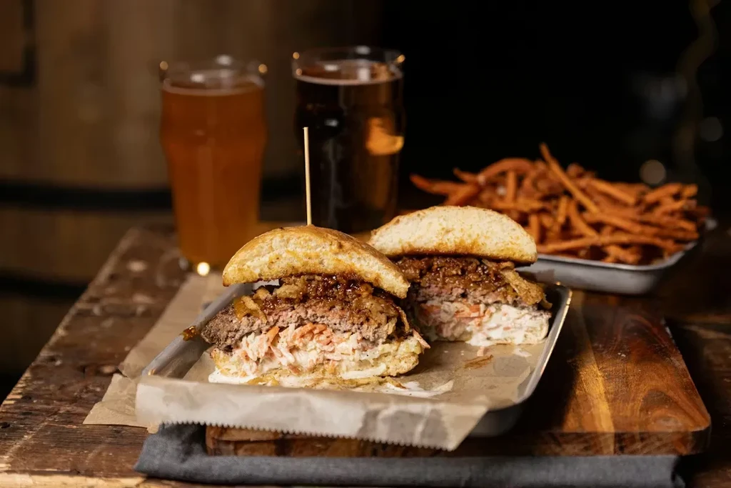 Gourmet burgers, sweet potato fries, and beer on a rustic table.