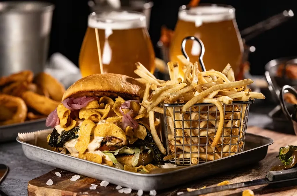 Close-up of a burger with chips, fries, and blurred beer glasses.
