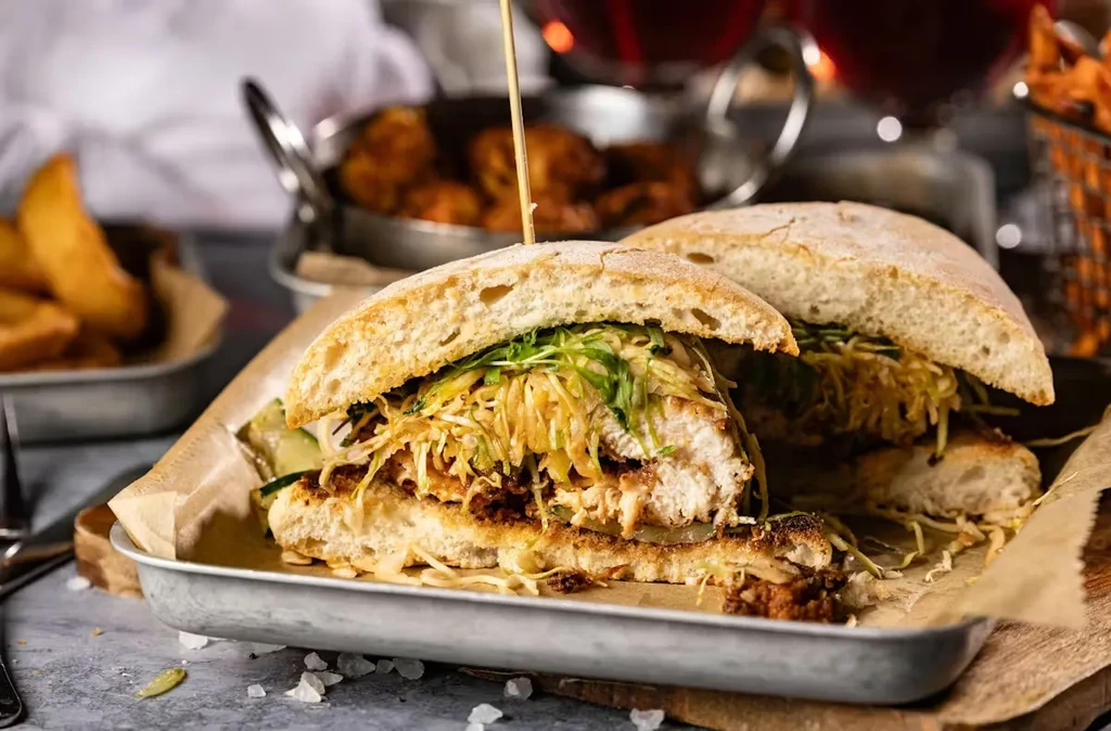 Rustic ciabatta sandwich with crispy fried protein, slaw, and greens.