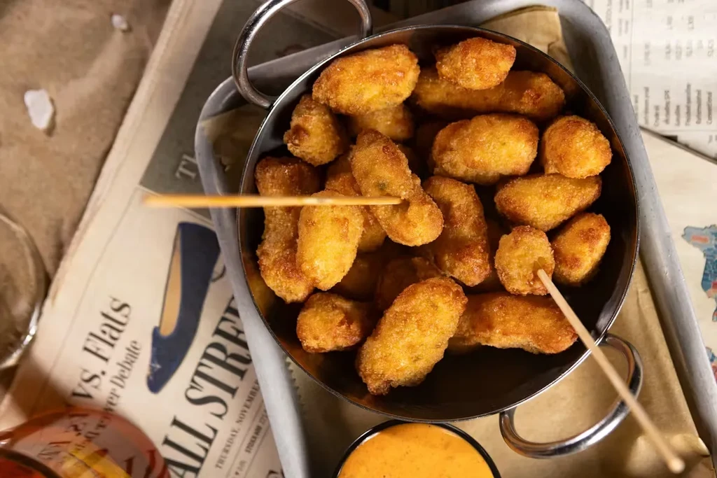 Deep-fried food with skewers in a pot on newspaper, dipping sauce.
