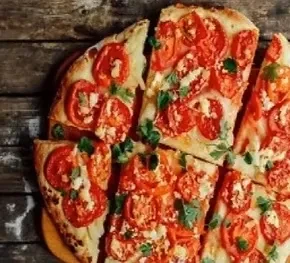Close-up of sliced pizza with tomatoes, cheese, and herbs on wood.