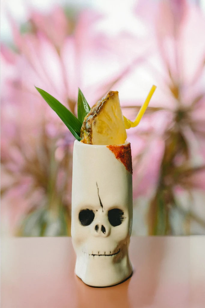 White ceramic skull mug cocktail with pineapple, leaves, and straw.