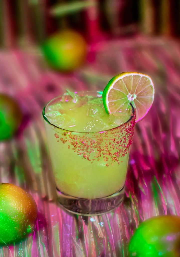 Colorful green cocktail with pink rim and lime garnish.