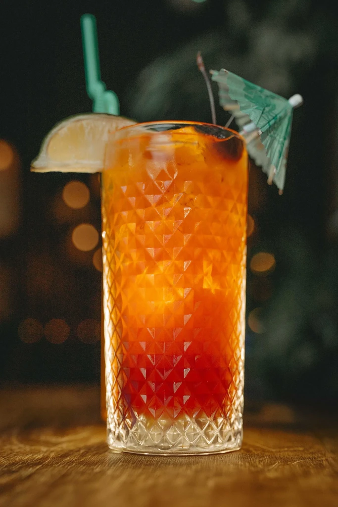 Orange gradient cocktail in faceted glass with lime, straw, and umbrella.