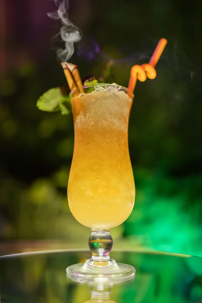 Amber cocktail with crushed ice, mint, and a smoking garnish.