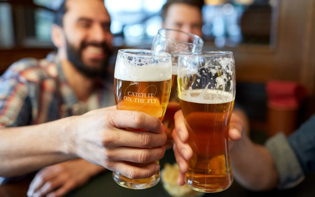 Three hands toast with beer glasses, one etched "CATCH IT ON THE FLY."