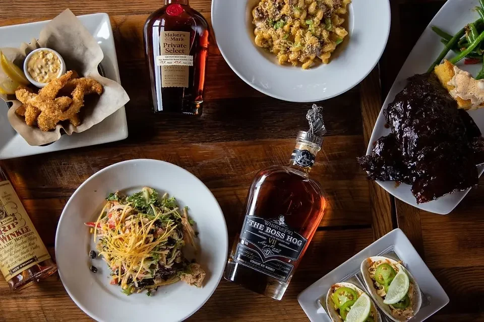 Flat lay of diverse food and premium spirits on a rustic table.