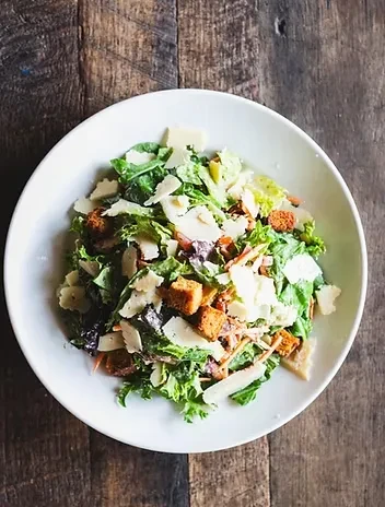 Top-down view of a vibrant green salad with croutons and Parmesan.