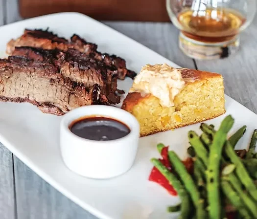 Smoked meat, cornbread, green beans, and BBQ sauce on a white plate.