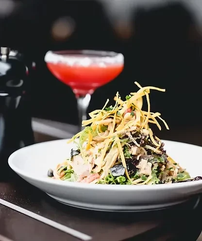 Artfully arranged salad, crispy topping, and a red cocktail.