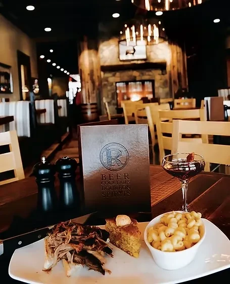 Rustic restaurant table with pulled pork, sides, cocktail, menu.