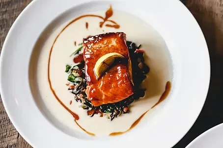 Plated glazed salmon, lemon, rice, vegetables, decorative sauces.