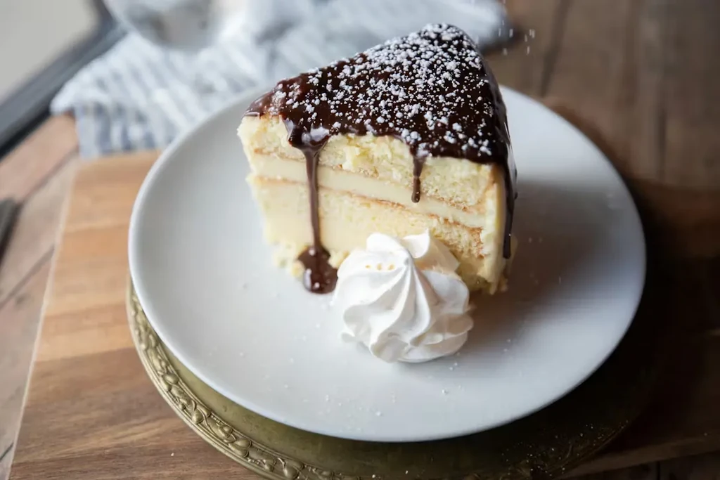 Close-up of layered cake slice with chocolate, whipped cream, gold charger.