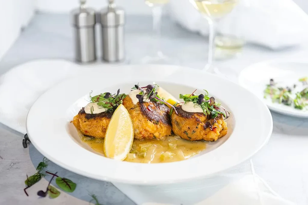 Three golden-brown patties topped with sauce, microgreens, and lemon.