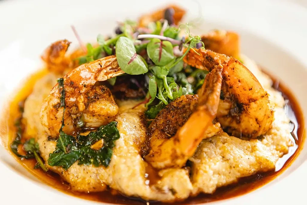 Seasoned shrimp and creamy grits garnished with microgreens and sauce.
