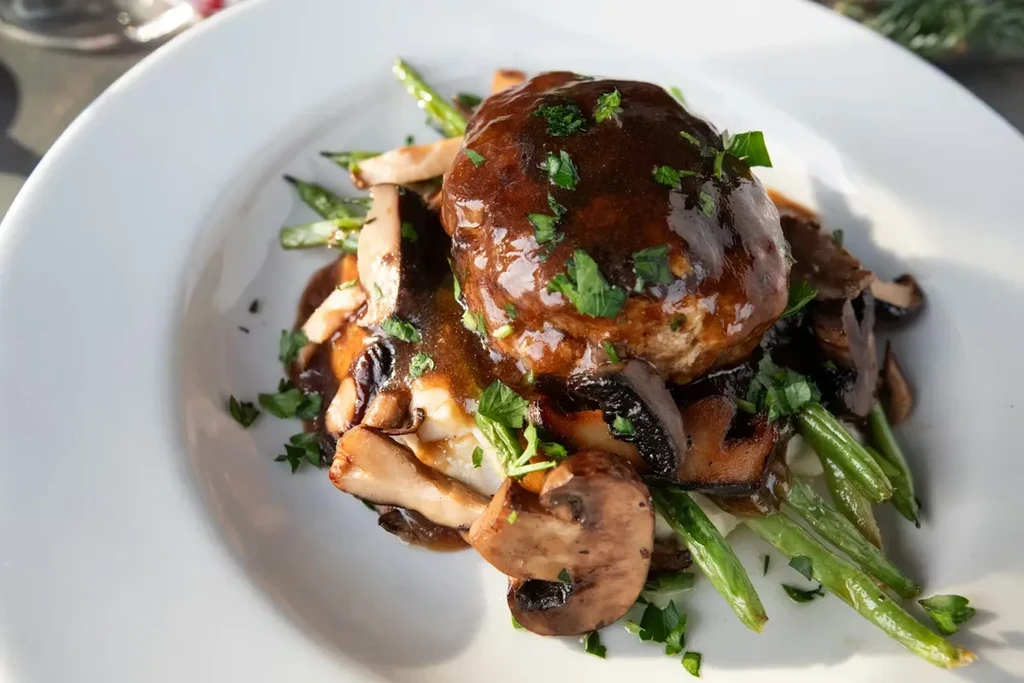 Plated meatloaf with dark gravy, parsley, mushrooms, and green beans.