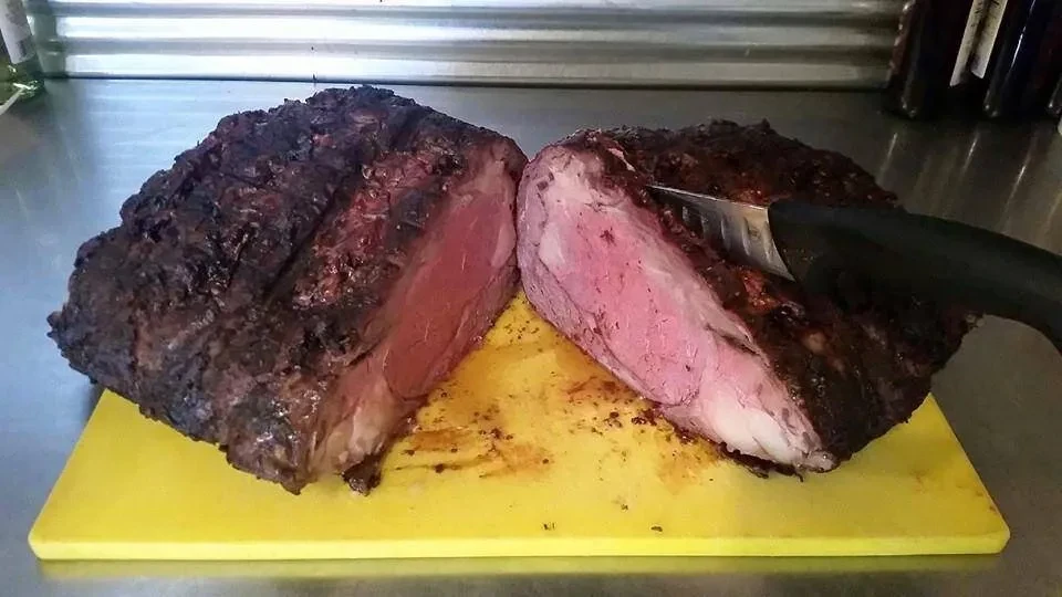Medium-rare roast, sliced, on yellow cutting board with serving tongs.