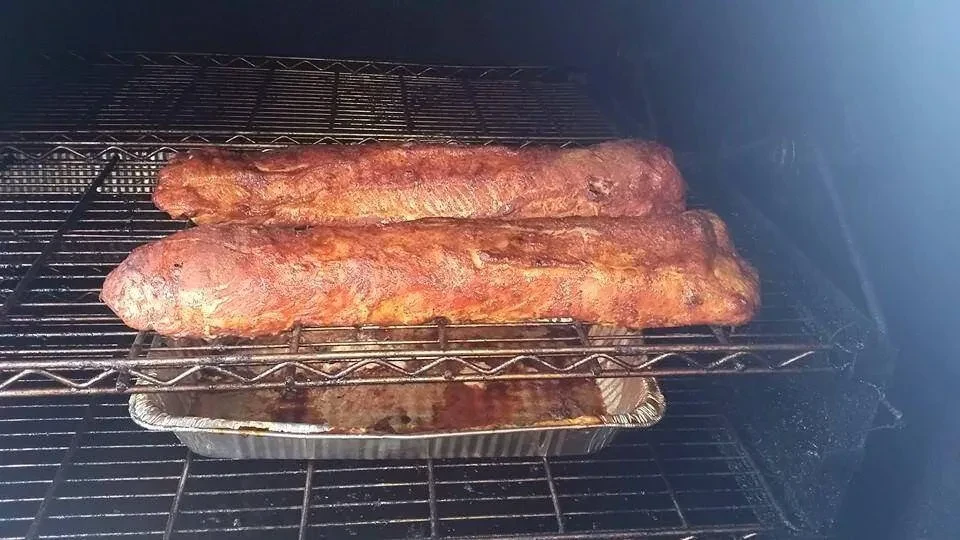 Two cuts of reddish-brown meat smoking inside a dark smoker.