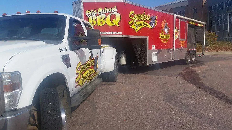 White Ford F-350 pulling red Squealer's Smoke Shack food trailer.