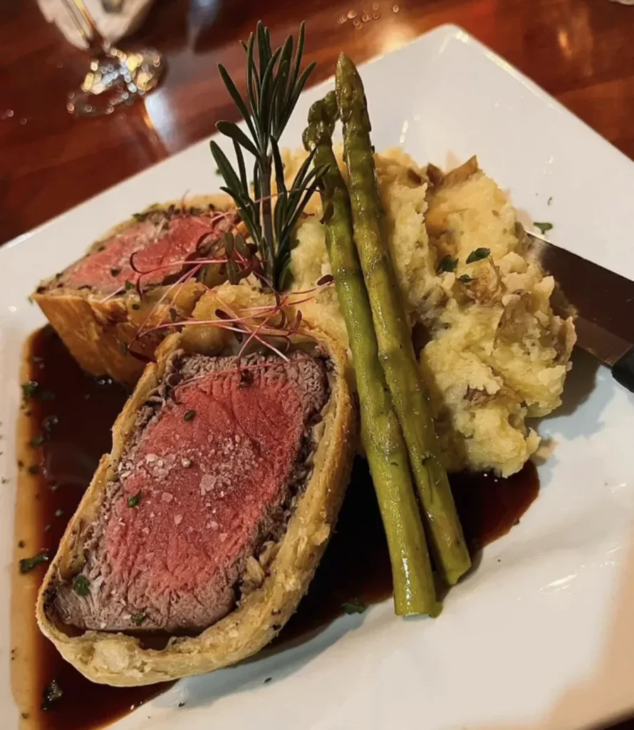 Plated Beef Wellington cut in half, with mashed potatoes and asparagus.