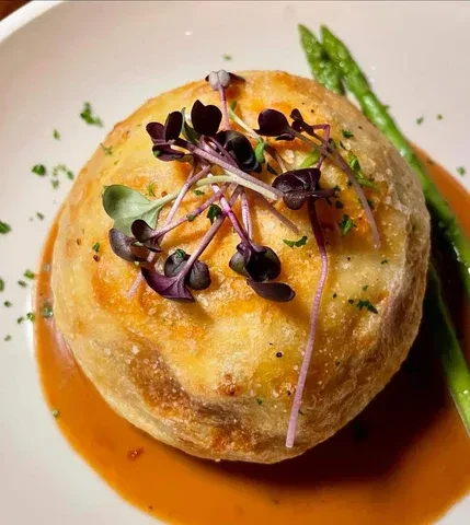 Plated savory pastry with golden crust, reddish sauce, microgreens, and asparagus.