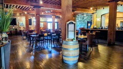 Warm, rustic-industrial restaurant interior with dining area, bar, and tree mural.