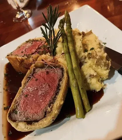 Sliced medium-rare Beef Wellington, mashed potatoes, asparagus, and sauce.