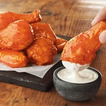 Hand dipping a buffalo chicken drumette into creamy white sauce.