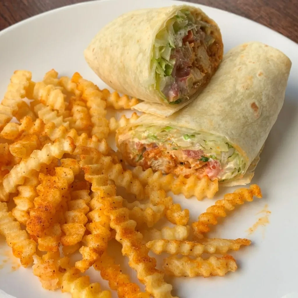 Sliced chicken wrap with lettuce, tomato, and seasoned crinkle fries.