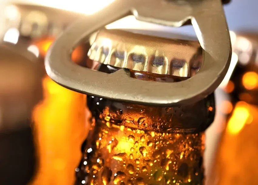 A cold, condensation-covered beer bottle being opened by an opener.