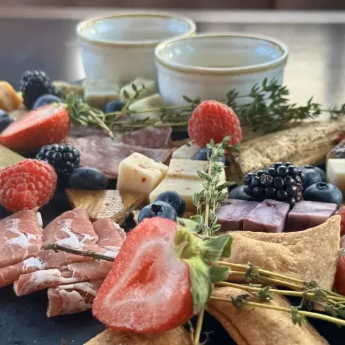 Close-up charcuterie board with berries, colorful cheeses, meats, herbs.