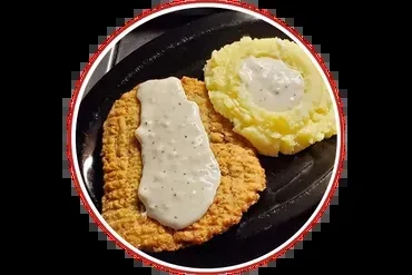 Chicken fried steak with gravy and mashed potatoes on a black plate.