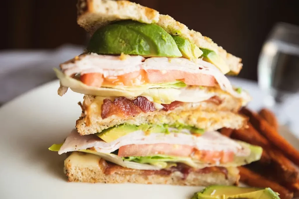 Stacked club sandwich with turkey, bacon, avocado, and sweet potato fries.
