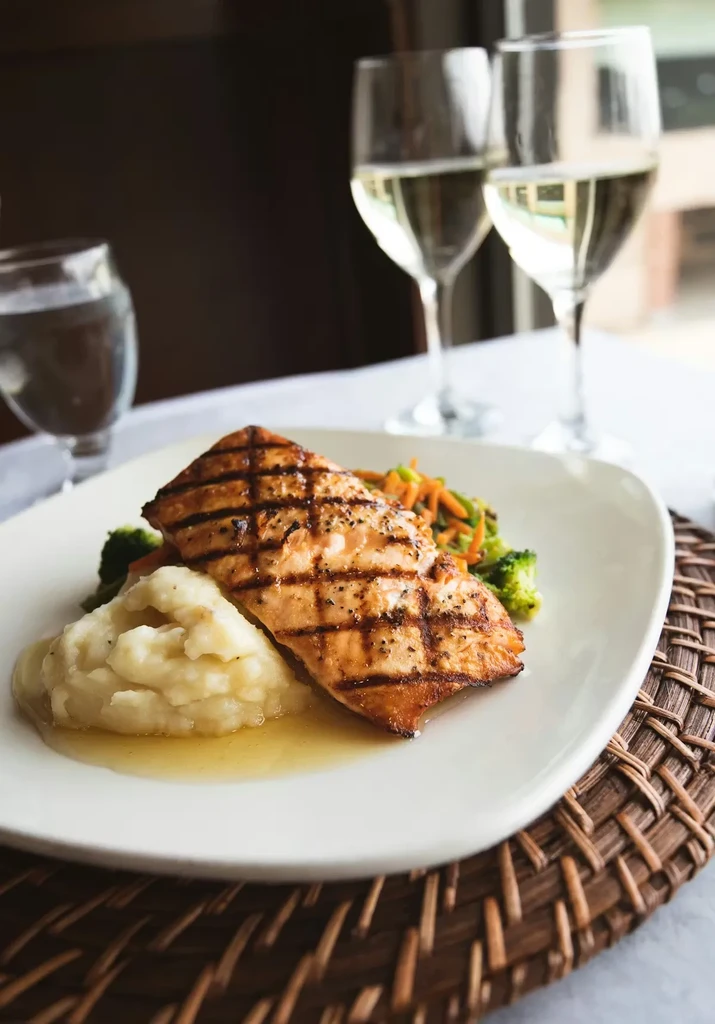 Plated grilled salmon, mashed potatoes, steamed vegetables, and white wine.