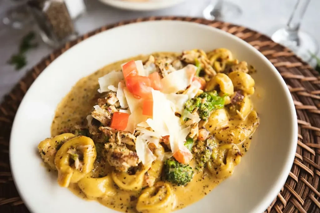 Close-up of creamy pasta with chicken, broccoli, tomatoes, Parmesan.