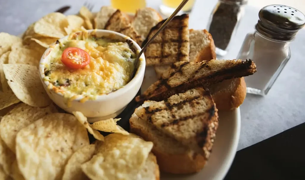 Creamy cheesy dip with tortilla chips, grilled bread, and tomato.