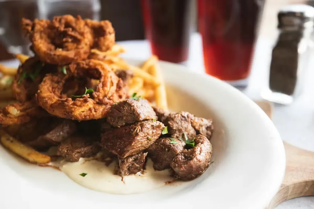 Herb-topped steak bites, golden onion rings, and fries with creamy sauce.