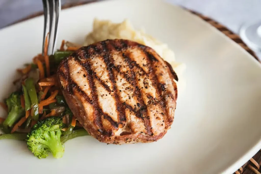 Close-up of grilled meat, mashed potatoes, and colorful vegetables.
