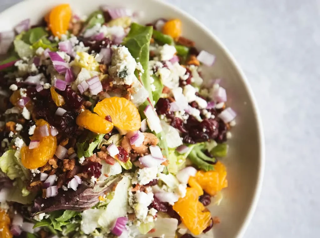 Colorful salad with greens, mandarin oranges, cheese, cranberries, and bacon bits.