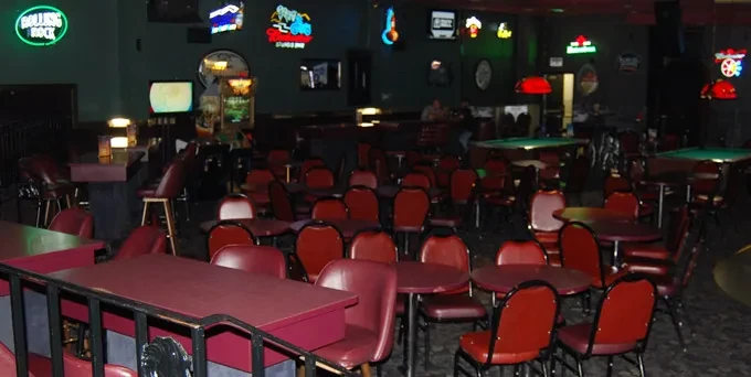 Dimly lit bar with tables, pool tables, and neon beer signs.